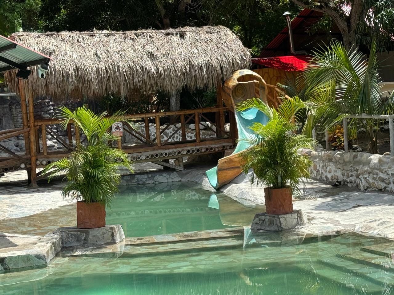 Piscina con tobogán y puente bajo techo de palma